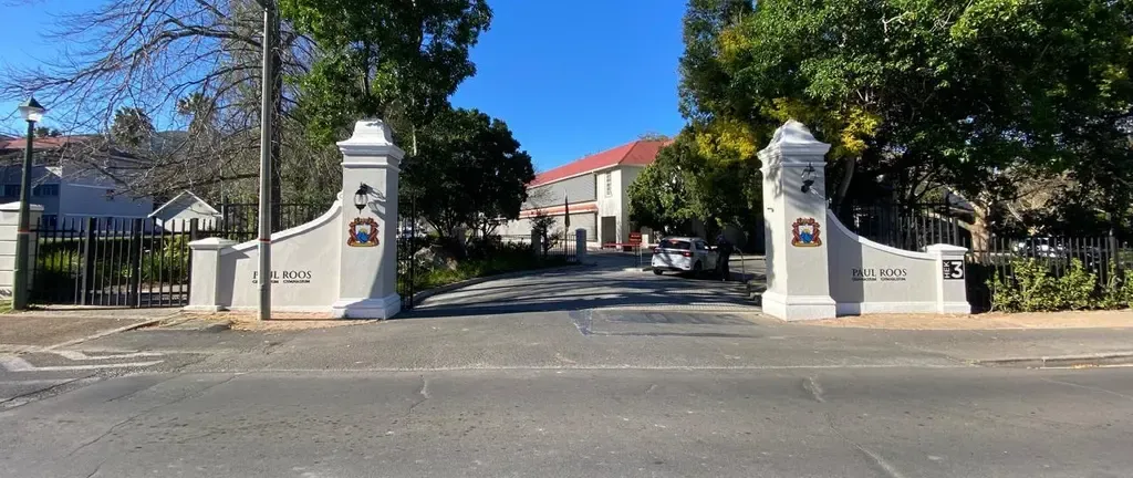 The Paul Roos Gymnasium gate on Noordwal-Wes Road: two white pillars either side of a driveway, PAUL ROOS lettered along the low wall, and a black HEK 3 plaque on the right-hand pillar.