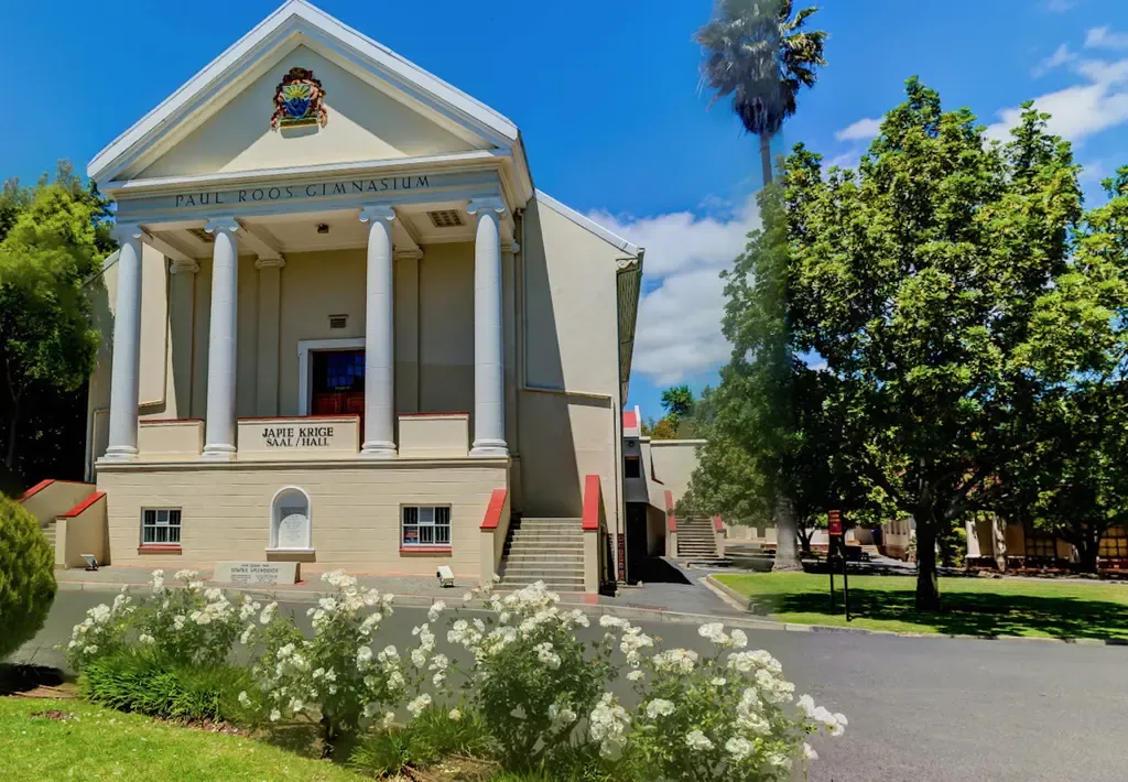 The front of the Japie Krige Hall from close up, with the road running past its right-hand side towards two flights of steps behind the building.